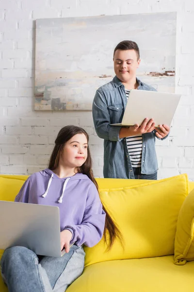 Amigos adolescentes con síndrome de Down usando computadoras portátiles en la sala de estar - foto de stock