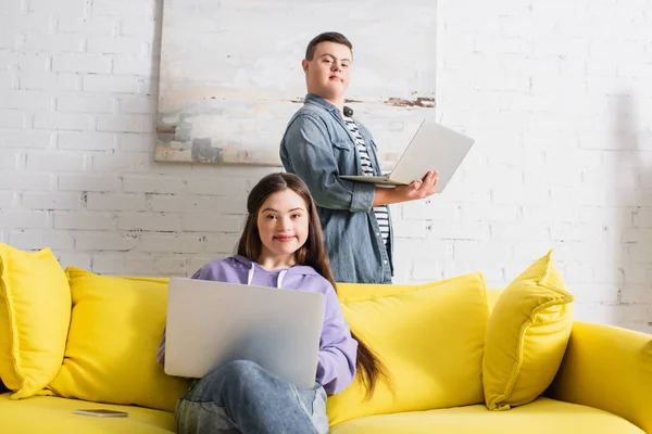 Adolescente sorridente com síndrome de down usando laptop perto de amigo em casa — Fotografia de Stock