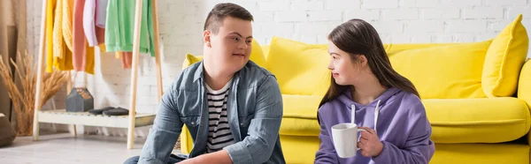 Adolescente sorridente con sindrome di Down guardando l'amico con tazza a casa, striscione — Foto stock