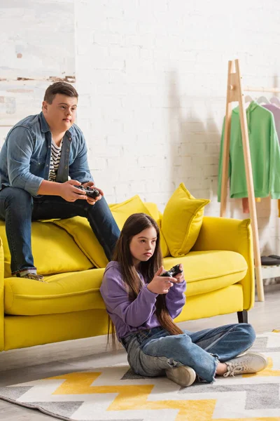 KYIV, UKRAINE - JANUARY 21, 2022: Teen friend with down syndrome playing video game in living room — Stock Photo