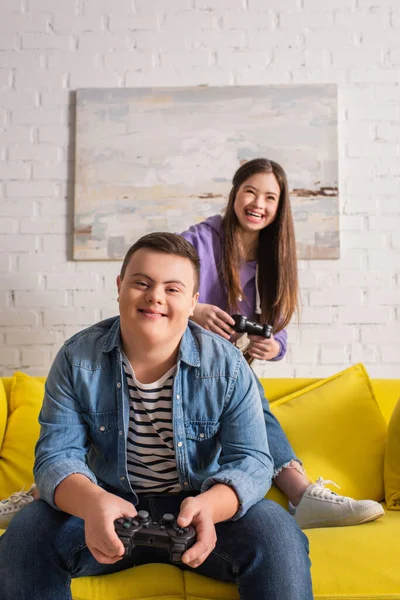 KYIV, UKRAINE - JANUARY 21, 2022: Smiling boy with down syndrome playing video game with blurred friend at home — Stock Photo