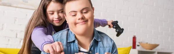 QUIIV, UCRÂNIA - JANEIRO 21, 2022: Adolescente com síndrome de down segurando joystick borrado perto de amigo em casa, banner — Fotografia de Stock