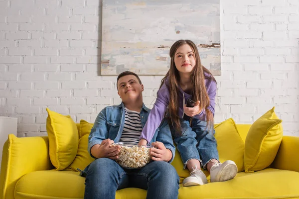 Teenagers with down syndrome holding popcorn while watching tv at home — Stock Photo