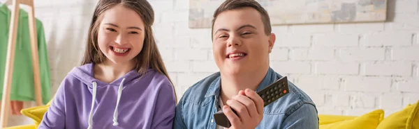 Adolescents positifs avec syndrome du duvet tenant télécommande à la maison, bannière — Photo de stock