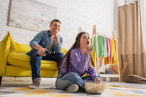 Teenager with down syndrome holding popcorn near friend on couch at home — Stock Photo