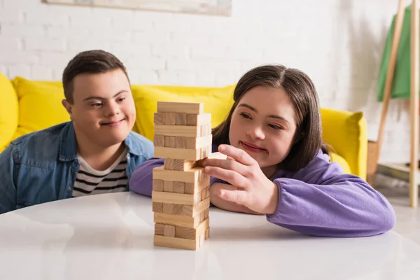 Sorrindo menina adolescente com síndrome de down jogando blocos de madeira jogo perto de amigo em casa — Fotografia de Stock
