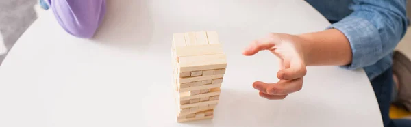 Cropped view of teenager playing wood blocks game on coffee table at home, banner — Stock Photo