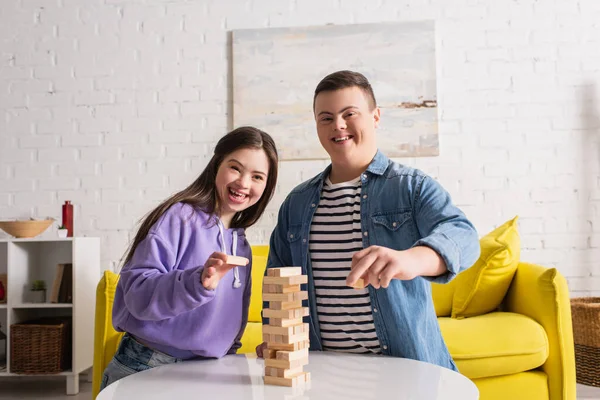 Amis heureux avec le syndrome du duvet regardant la caméra près de blocs de bois jeu à la maison — Photo de stock