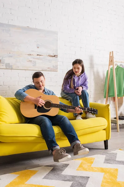 Teenager with down syndrome playing acoustic guitar near friend at home — Stock Photo