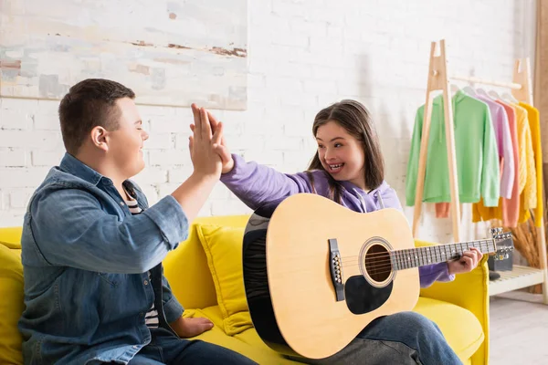 Adolescentes positivos com síndrome de down dando alta cinco perto de guitarra acústica em casa — Fotografia de Stock