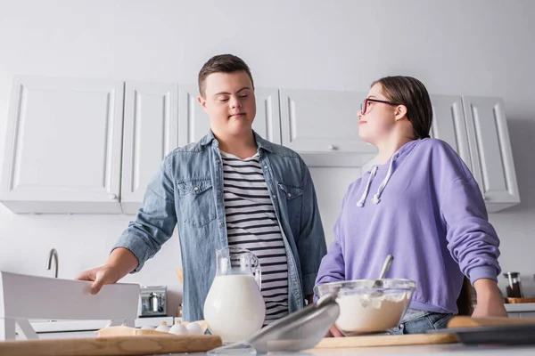 Low angle view of couple with down syndrome standing near ingredients in kitchen — Stock Photo