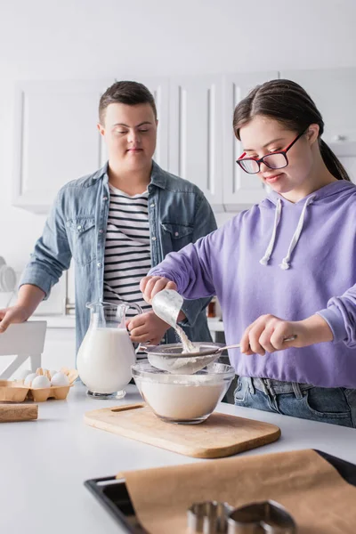 Adolescente con síndrome de Down cocinando cerca de la comida y amigo en la cocina - foto de stock