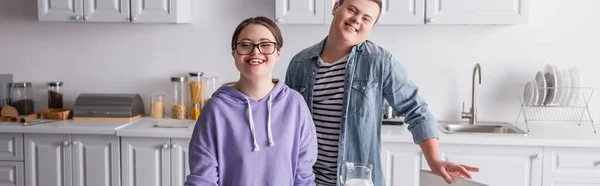 Positive teenagers with down syndrome looking at camera in kitchen, banner — Stock Photo