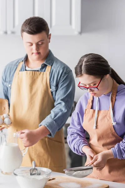Teenager mit Down-Syndrom kocht in der Nähe von Mehl und verschwommenem Freund in Küche — Stockfoto