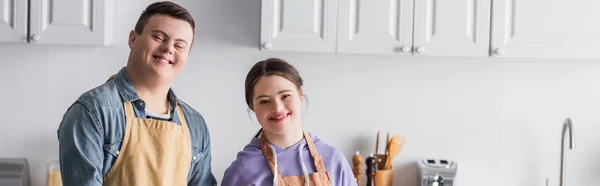 Smiling teenagers with down syndrome looking at camera in kitchen, banner — Stock Photo