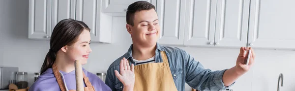 Adolescents positifs atteints du syndrome du duvet ayant un appel vidéo sur téléphone portable dans la cuisine, bannière — Photo de stock