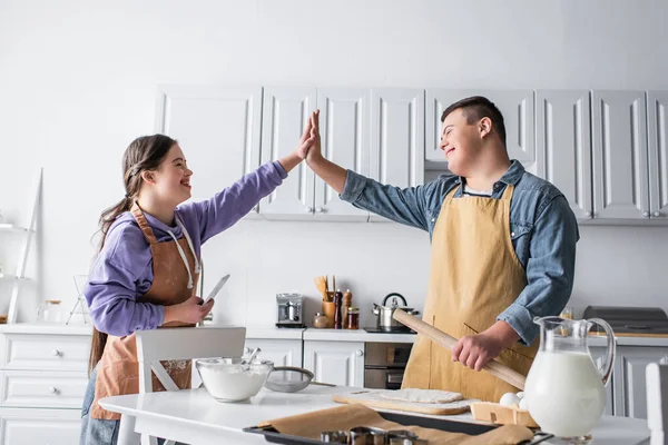 Amis positifs avec le syndrome du duvet donnant haute cinq près de la nourriture dans la cuisine — Photo de stock