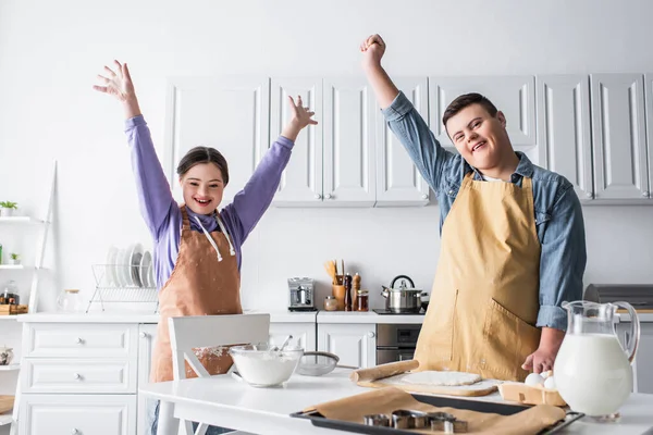 Amigos emocionados con síndrome de Down de pie cerca de la comida en la cocina - foto de stock