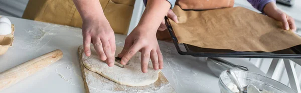 Cropped view of teenager making cookie near friend with baking sheet at home, banner — Stock Photo