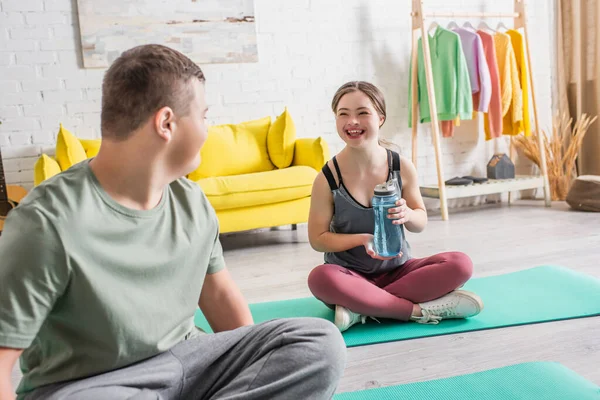 Positivo adolescente chica sosteniendo botella de deportes cerca de amigo en casa - foto de stock