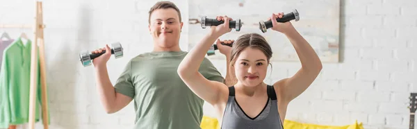 Adolescente com síndrome de down treinamento com halteres perto de amigo em casa, banner — Fotografia de Stock