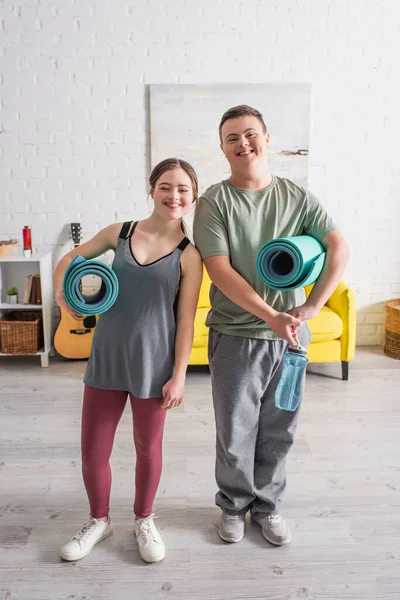 Adolescents heureux avec le syndrome du duvet tenant bouteille de sport et tapis de fitness à la maison — Photo de stock