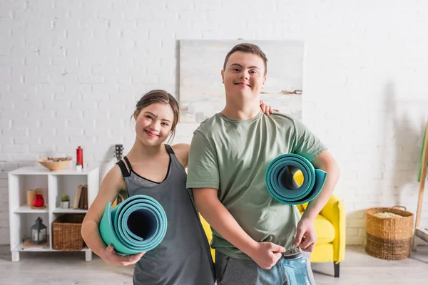 Positive teen couple with down syndrome holding fitness mats at home — Stock Photo