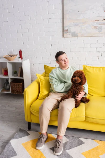 Fröhlicher Junge mit Down-Syndrom streichelt Pudel zu Hause auf Couch — Stockfoto