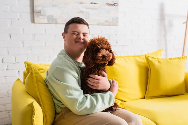 Счастливый подросток с синдромом Дауна, обнимающий пуделя на диване — стоковое фото