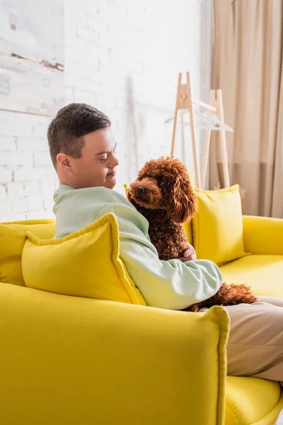 Teenager with down syndrome looking at brown poodle in living room — Stock Photo