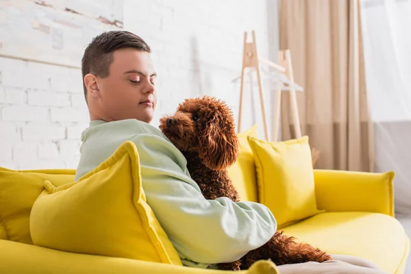 Adolescente com síndrome de down abraçando poodle no sofá amarelo — Fotografia de Stock