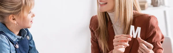 Terapeuta del habla positiva sosteniendo carta cerca del niño en la sala de consulta, pancarta — Stock Photo