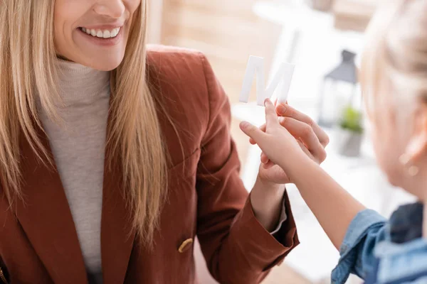 Cropped view of blurred kid pointing at letter near smiling speech therapist in consulting room — Stock Photo
