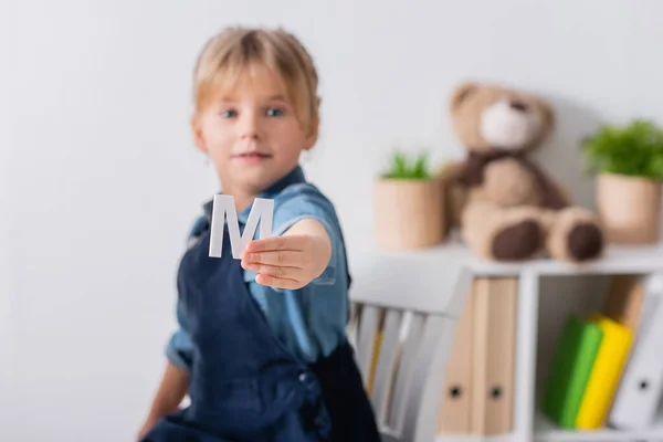 Blurred child holding letter and looking at camera in classroom — Stock Photo