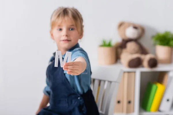 Enfant flou tenant une lettre et regardant la caméra en classe — Photo de stock