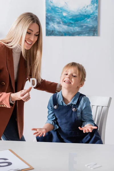 Terapeuta positivo del habla sosteniendo carta cerca del niño en la sala de consulta - foto de stock