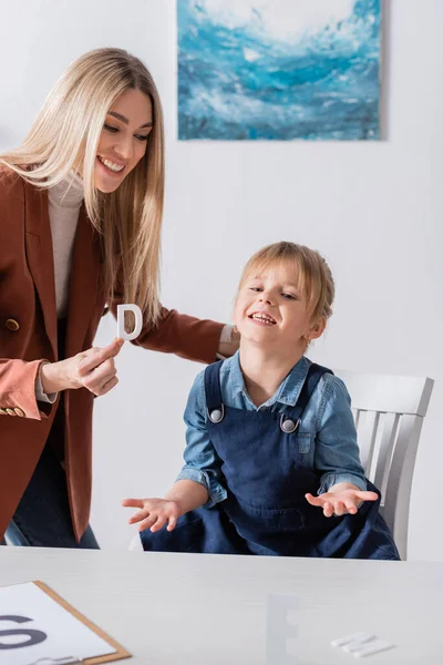 Orthophoniste positif tenant une lettre près de l'enfant dans la salle de consultation — Photo de stock