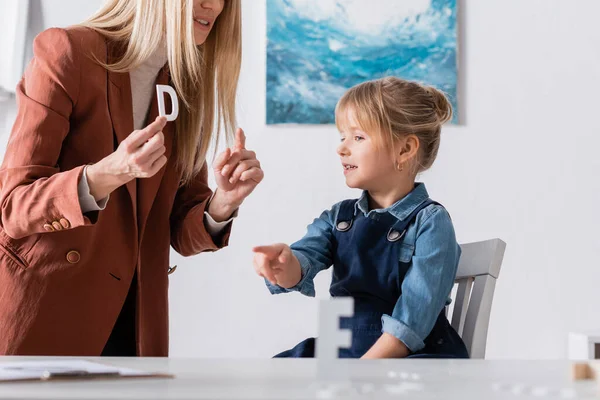 Speech therapist pointing at letter near girl in consulting room — Stock Photo