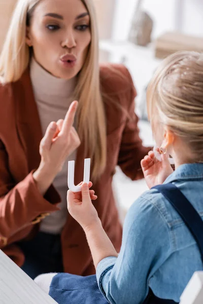 Enfant flou tenant une lettre près d'un orthophoniste faisant un geste dans une salle de consultation — Photo de stock