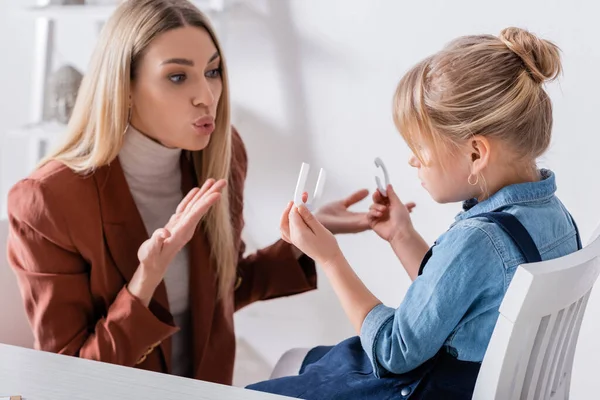 Terapeuta del habla hablando cerca de un niño con cartas en la sala de consulta — Stock Photo