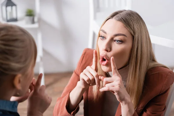 Terapeuta del habla gesticulando y hablando cerca de chica borrosa en el aula - foto de stock