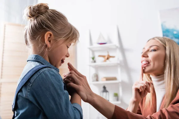 Blurred speech therapist pointing at mouth during lesson with pupil in classroom — стоковое фото