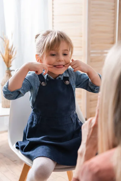 Niño sobresaliendo lengua cerca del terapeuta del habla en el aula - foto de stock