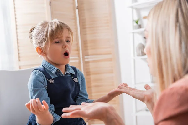 Chica hablando durante la lección con logopedista borrosa en el aula - foto de stock