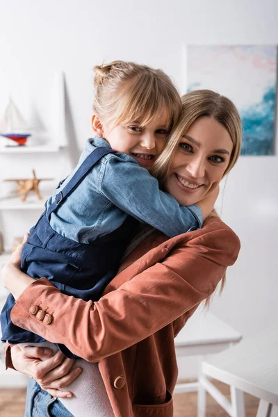 Positive speech therapist hugging pupil and looking at camera in classroom — Stock Photo