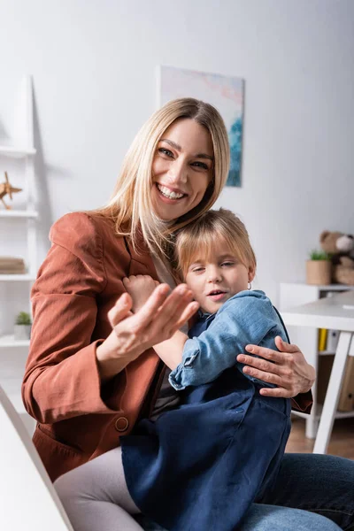 Terapeuta del habla positiva señalando con la mano y abrazando al alumno en el aula — Stock Photo