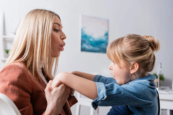 Side view of speech therapist and pupil grimacing and holding hands in classroom — Stock Photo