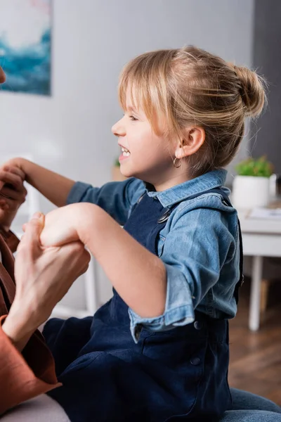 Side view of child grimacing and holding hands of speech therapist in classroom — Stock Photo