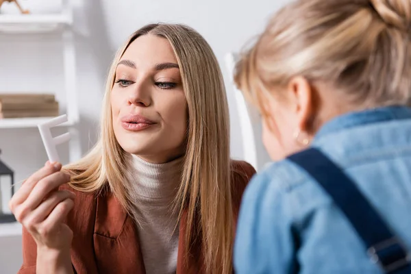 Terapeuta del habla mirando la carta cerca de chica borrosa en el aula - foto de stock