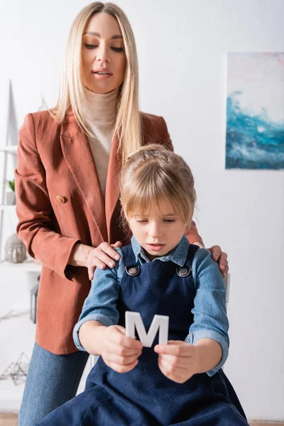 Ragazza che tiene lettera vicino logopedista in classe — Foto stock